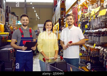 Seller and happy couple of buyers who buy tools for repair in hypermarket of building materials. Stock Photo