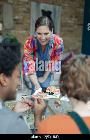 Happy woman serving sushi to friends Stock Photo