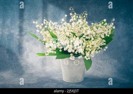 Bouquet of lily of the valleys in a vase on a blue backdrop. Holiday background. Selective focus, copy space for text Stock Photo