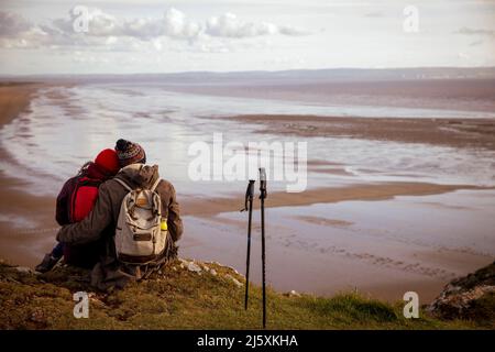 Affectionate couple taking a break from hike on cliff over beach Stock Photo