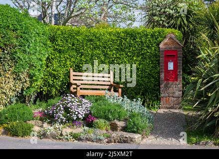Rectangular red Royal Mail post box or letter box installed in a brick pillar next to wooden bench as a nice please to sit in West Sussex, England, UK Stock Photo