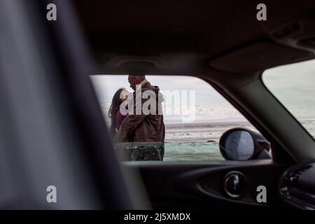 Affectionate couple hugging outside car on beach Stock Photo