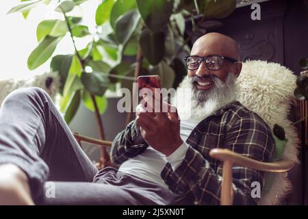 Happy senior man using smart phone in armchair Stock Photo