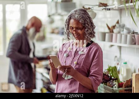 Senior woman using smart phone in kitchen Stock Photo