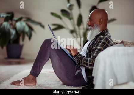 Mature man with beard using laptop on floor Stock Photo