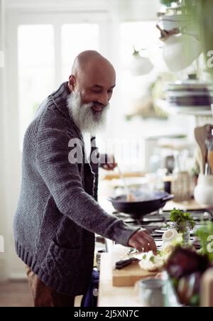 Smiling man with beard cooking in kitchen Stock Photo