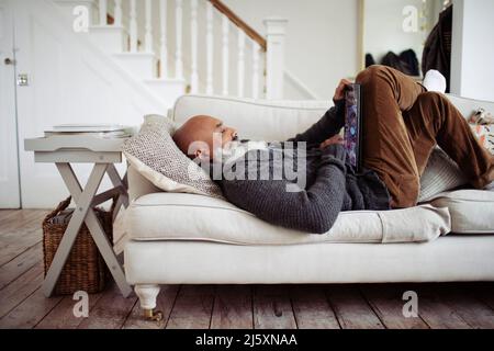 Mature man relaxing on living room sofa with digital tablet Stock Photo