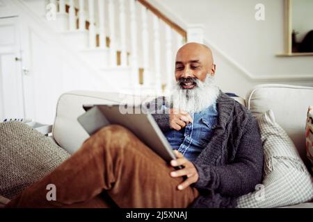 Mature man with beard using digital tablet on living room sofa Stock Photo