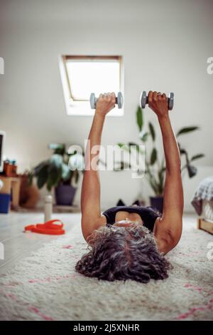 Senior woman exercising with dumbbells on rug Stock Photo