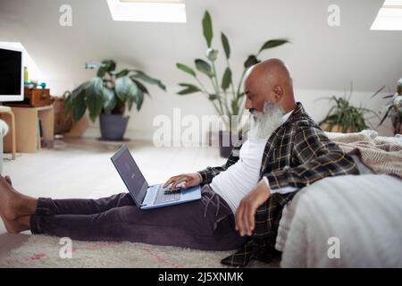 Mature man with beard using laptop on bedroom floor Stock Photo