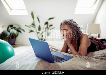 Senior woman using laptop on bed Stock Photo