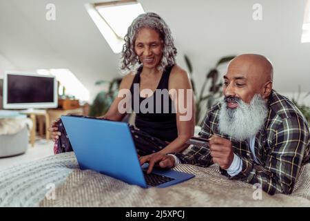 Happy senior couple with credit card using laptop on bed Stock Photo