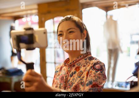 Female shop owner vlogging with smart phone in boutique Stock Photo