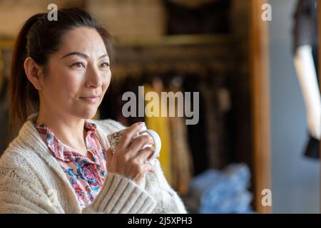 Female shop owner drinking coffee and looking away Stock Photo