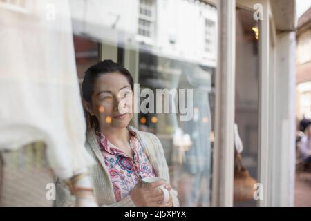 Female shop owner drinking tea at shop window Stock Photo