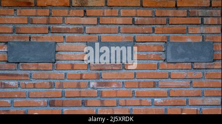 Old red brick wall with 3 black concrete blocks in center background texture Stock Photo