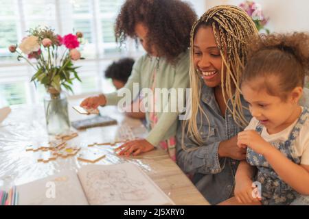 Happy mother and daughters coloring and playing at table Stock Photo