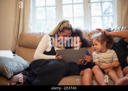 Mother and daughters using digital tablet on living room sofa Stock Photo