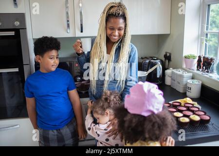 Happy mother and kids baking cupcakes in kitchen Stock Photo
