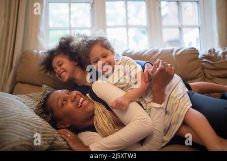 Happy playful mother and daughters on living room sofa Stock Photo