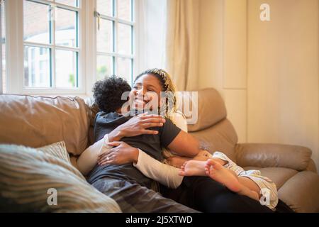 Happy mother and son hugging on living room sofa Stock Photo