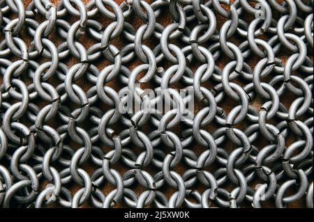 Flat lay view of chain mail armor on brown leather. Metallic background. Stock Photo