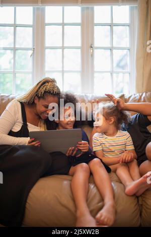 Mother and daughters using digital tablet on living room sofa Stock Photo