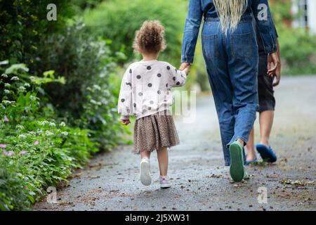 Mother and daughter holding hands walking on driveway Stock Photo
