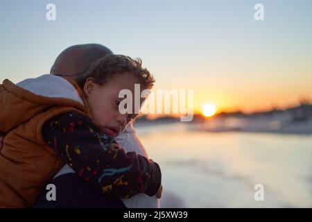 Portrait boy with Down Syndrome on father shoulder on beach at sunset Stock Photo