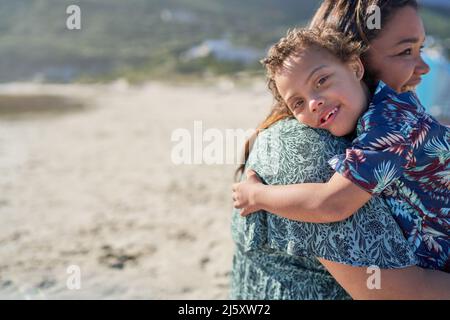 Portrait happy boy with Down Syndrome over shoulder of mother on beach Stock Photo