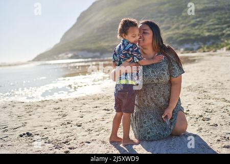 Happy mother hugging cute son on sunny summer beach Stock Photo