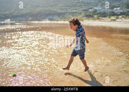 Carefree boy with Down Syndrome running and splashing in ocean surf Stock Photo