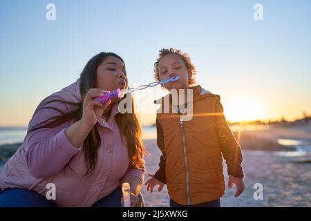 Mother and son with Down Syndrome blowing bubbles on beach Stock Photo