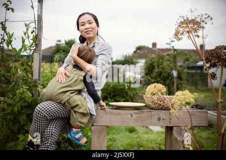 Portrait happy mother holding tired toddler son on garden bench Stock Photo