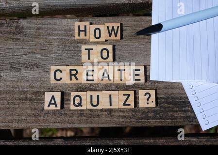 How to create a quiz? Black capital letter words on wooden toy blocks on a natural garden table background with paper and pencil. Perfect for websites. Stock Photo