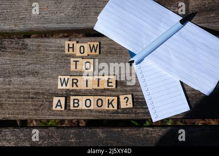 How to write a book? Black capital letter words on wooden toy blocks on a natural garden table background with paper and pencil. Perfect for websites. Stock Photo