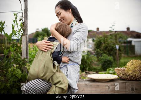 Happy mother holding toddler son on garden bench Stock Photo