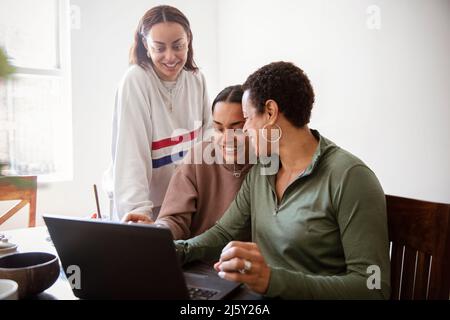 Happy mother and young adult daughters using laptop at home Stock Photo