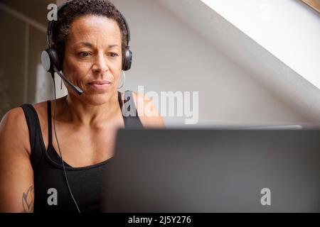 Mature woman in headset working from home at laptop Stock Photo