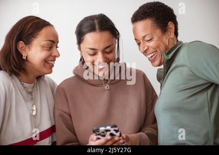 Happy mother and young adult daughters using smart phone Stock Photo