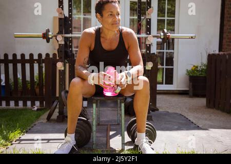 Woman taking a break from weightlifting on sunny patio Stock Photo