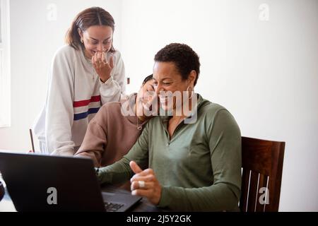 Happy mother and daughters using laptop in dining room Stock Photo