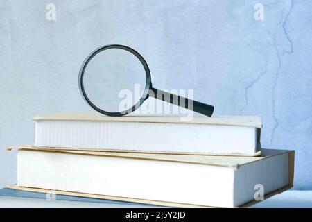 stack of books and magnifying glass on table. Stock Photo