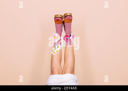 Legs of crop unrecognizable bride upside down in bright socks with colorful flowers on high heeled shoes on light background in studio Stock Photo