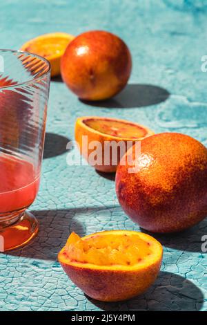 Halves of ripe tasty squeezed blood oranges placed on table with transparent glass of red juice in light room with sunshine Stock Photo