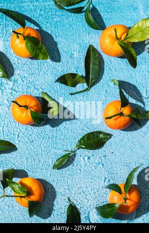 Top view full frame background of ripe tropical tangerines with leaves slices and skin on cracked bright blue surface Stock Photo