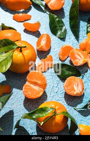 Top view full frame background of ripe tropical tangerines with leaves slices and skin on cracked bright blue surface Stock Photo