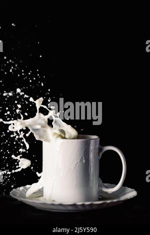 Ceramic mug on plate with flying splashes of milk on table against black background Stock Photo