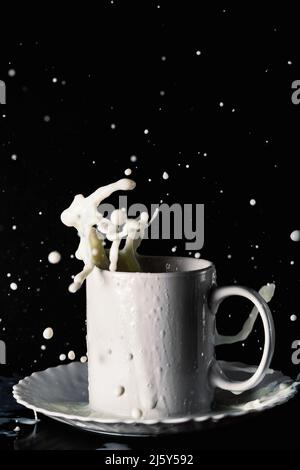 Ceramic mug on plate with flying splashes of milk on table against black background Stock Photo