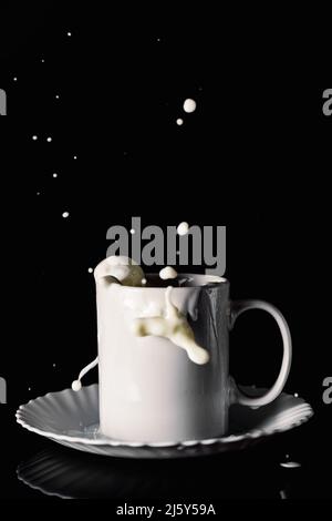 Ceramic mug on plate with flying splashes of milk on table against black background Stock Photo